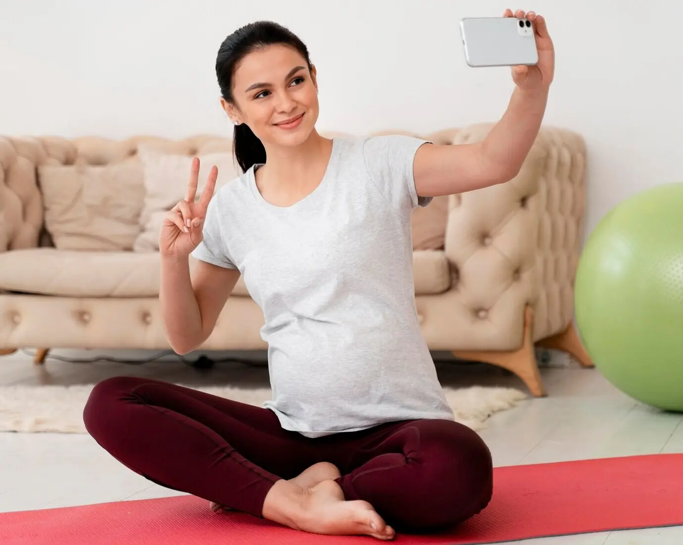 Schwangere Frau im Lotussitz, die ein Selfie macht.