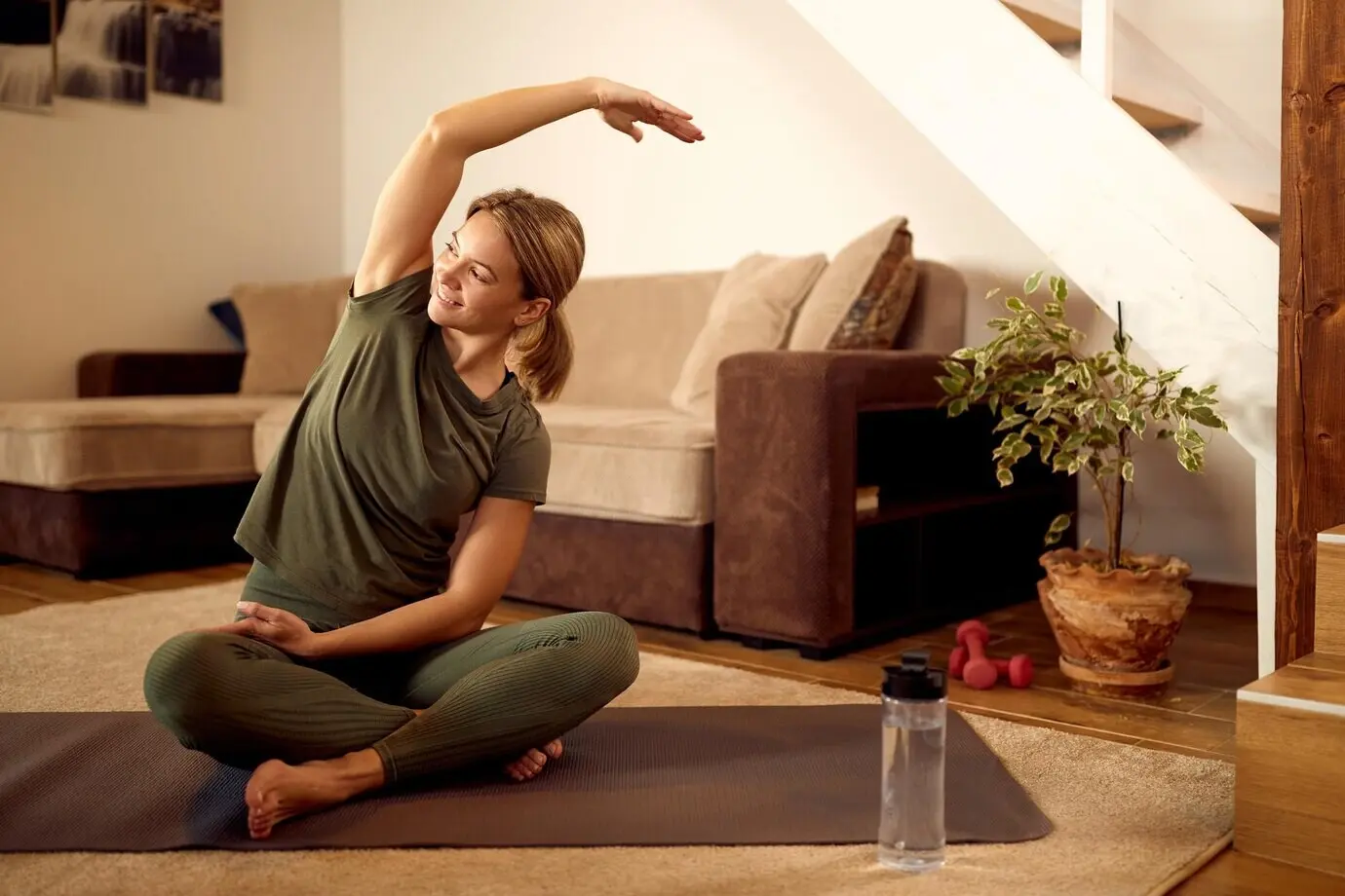 Fröhliche, athletische Frau macht Dehnübungen beim Heimtraining.